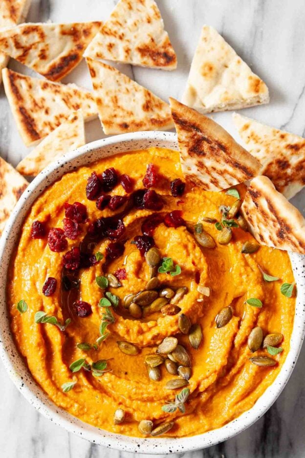 pumpkin hummus in a bowl, garnished with pepitas, dried cranberries, and pita chips.