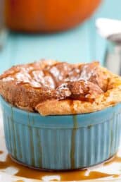 A baked pumpkin souffl&eacute; in a blue ramekin, topped with powdered sugar and drizzled with caramel sauce.