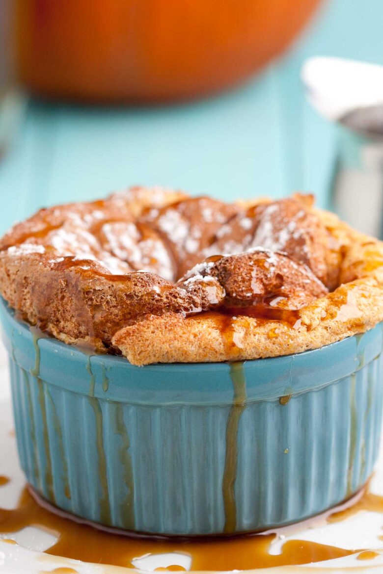 A baked pumpkin soufflé in a blue ramekin, topped with powdered sugar and drizzled with caramel sauce.