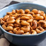 A blue bowl filled with roasted cashews seasoned with garlic and rosemary.