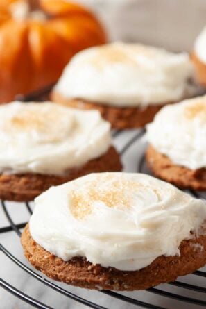Closeup shot of pumpkin cookies with cream cheese frosting on a wire rack.