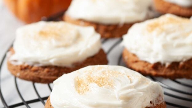 Closeup shot of pumpkin cookies with cream cheese frosting on a wire rack.