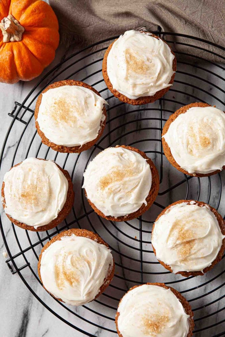 Overhead shot of pumpkin cookies with cream cheese frosting on a wire rack.