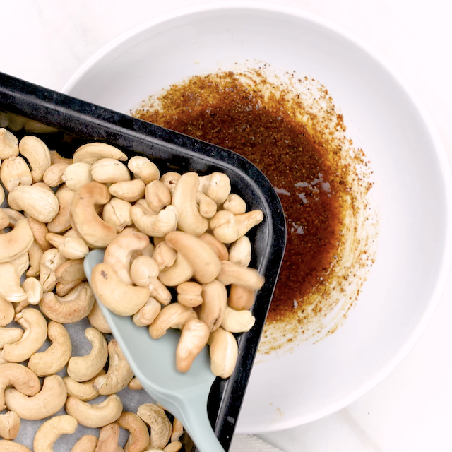 Warm cashews being added to spiced butter mixture to make roasted cashews.
