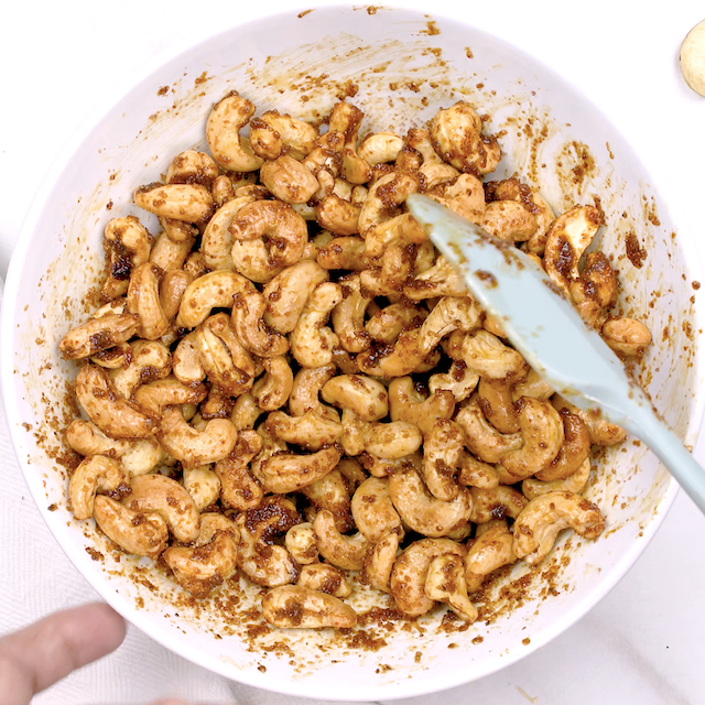 Roasted cashews being mixed with spiced butter.