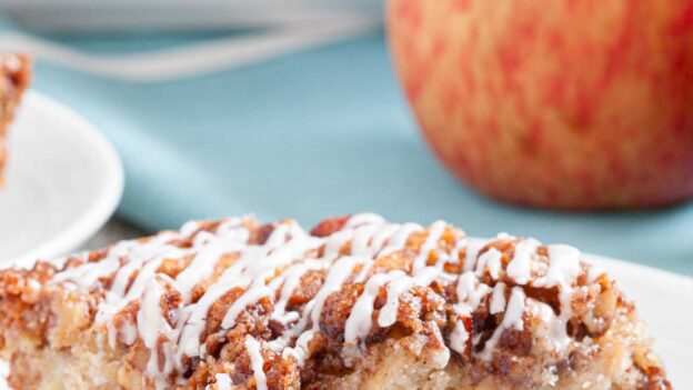 Closeup shot of a slice of apple coffee cake with pecan streusel topping and icing.