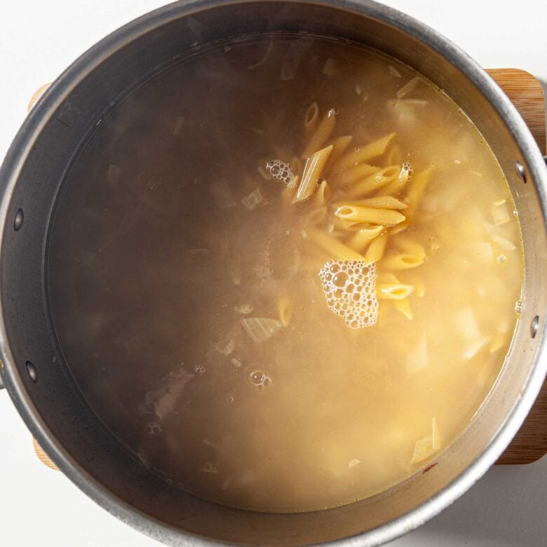 Pasta being boiled in broth to make butternut squash pasta at home.