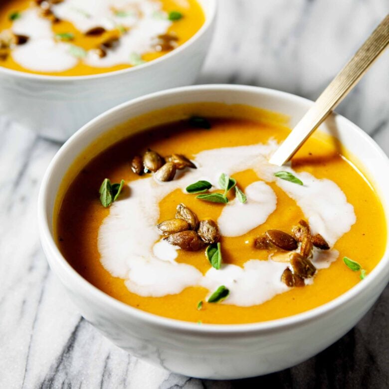 Curry butternut squash soup in a bowl with coconut milk on top, and garnished with fresh herbs and roasted pepitas.