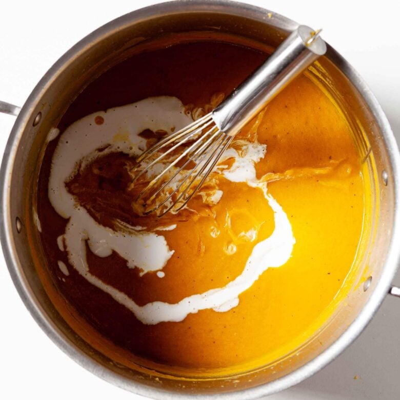 Curry butternut squash soup in a pot with coconut milk and a whisk.