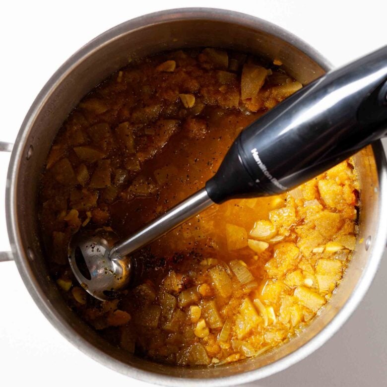 A pot with curry butternut squash being cooked and an immersion blender.