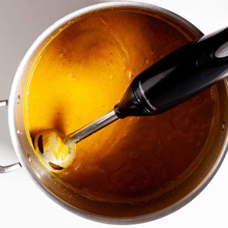 Curry butternut squash soup blended in a pot using an immersion blender.
