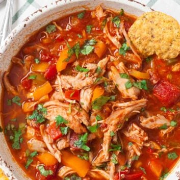 A bowl of healthy chicken chili with shredded chicken, diced tomatoes, bell peppers, and fresh herbs, garnished with crunchy tortilla chips.
