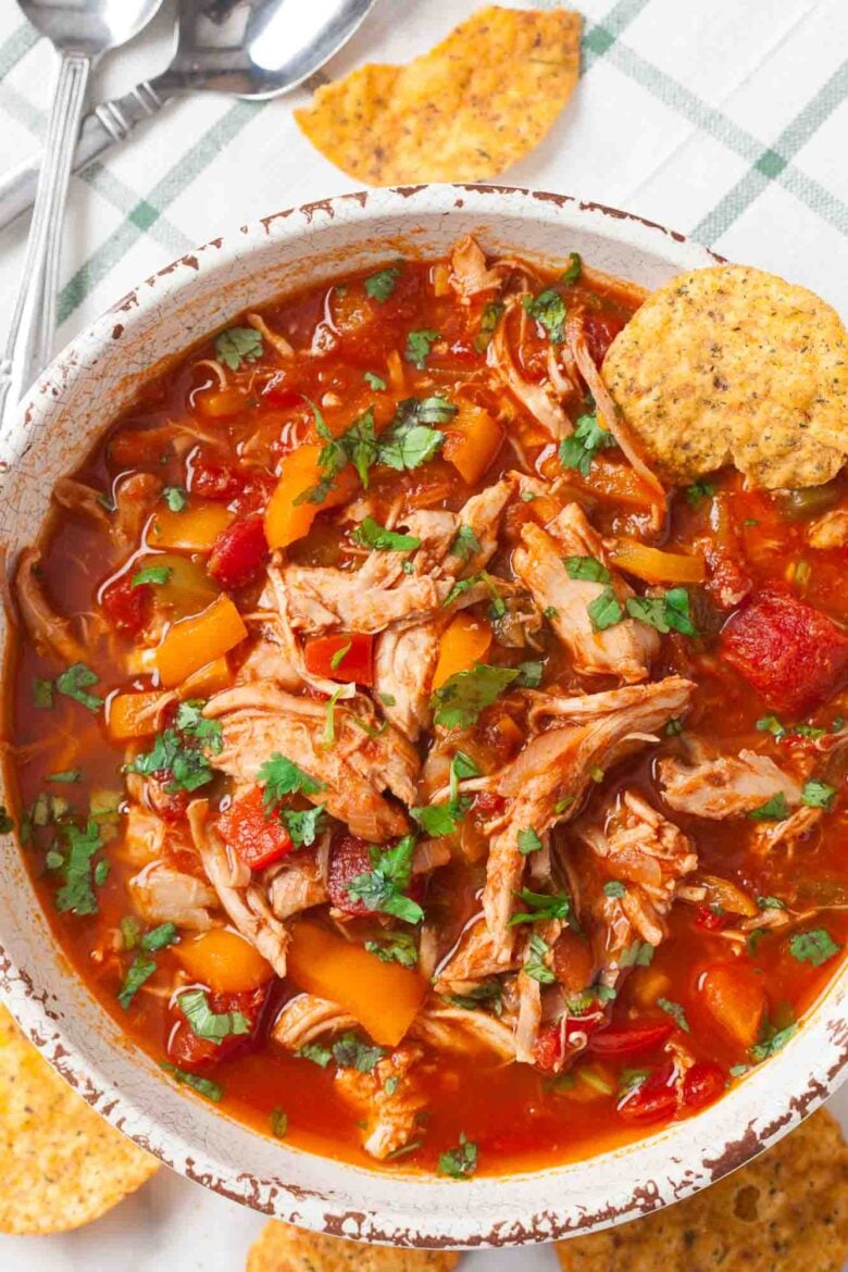 A bowl of healthy chicken chili with shredded chicken, diced tomatoes, bell peppers, and fresh herbs, garnished with crunchy tortilla chips.