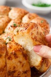 Closeup shot of a hand pulling apart a piece of pull-apart rolls with parmesan and garlic.