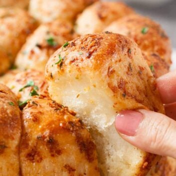 Closeup shot of a hand pulling apart a piece of pull-apart rolls with parmesan and garlic.