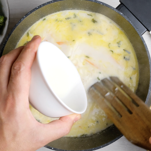 Cornstarch slurry being poured into broccoli cheese soup base in a pot.