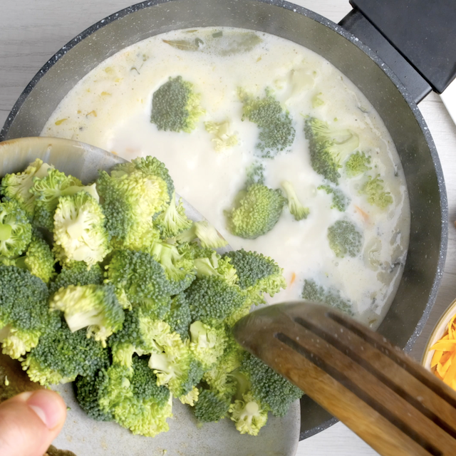 Broccoli florets being added to pot to make broccoli cheese soup at home.