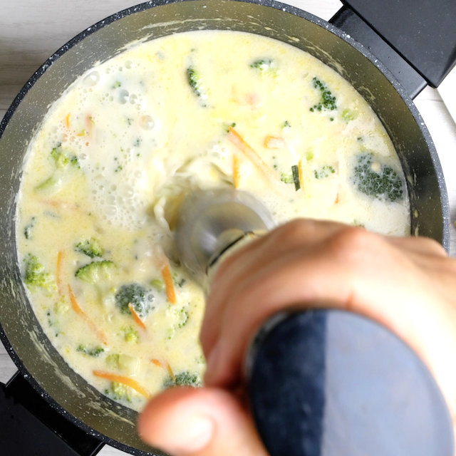 Broccoli cheese soup being blended with an immersion blender.