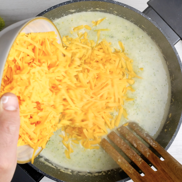 Shredded cheddar cheese being added to soup pot.