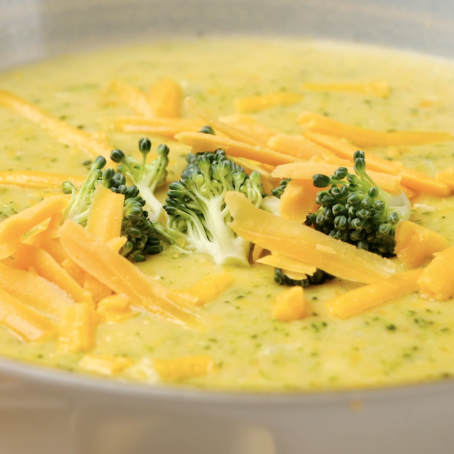 Freshly served broccoli cheese soup with broccoli florets and shredded cheddar on top.