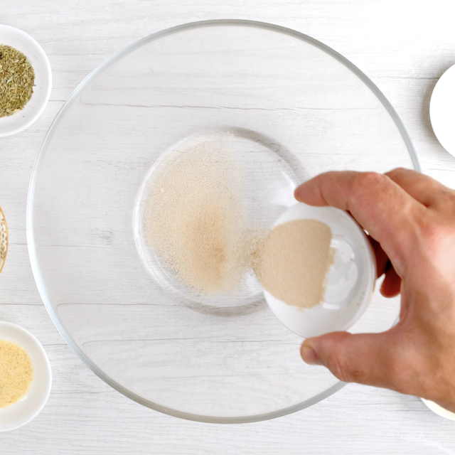 Yeast being sprinkled into a glass bowl with water.