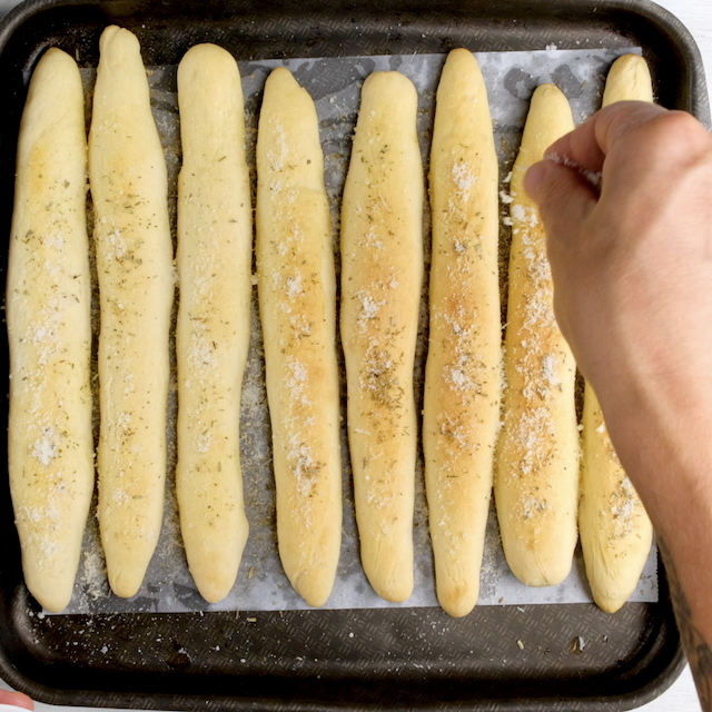 Topping mixture being sprinkled on hot freshly baked breadsticks.