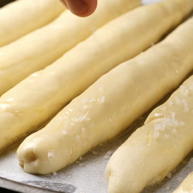 Kosher salt being sprinkled on unbaked breadsticks.