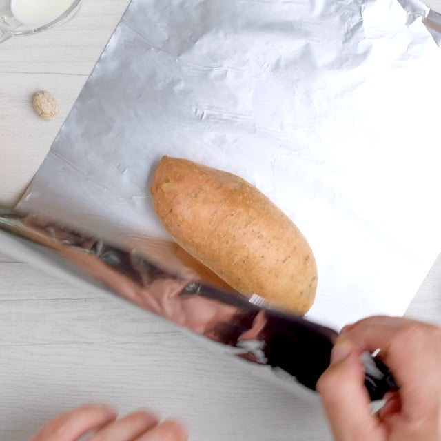 A sweet potato being covered with aluminum foil.