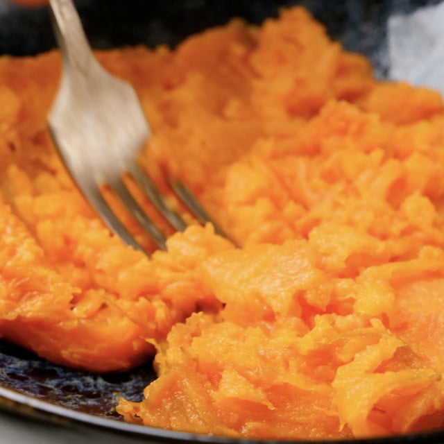 Roasted sweet potatoes being mashed with a fork to make sweet potato muffins.