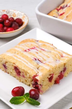 A slice of cranberry cake with fresh cranberries on the side.