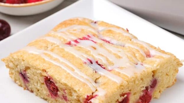 A slice of cranberry cake with fresh cranberries on the side.