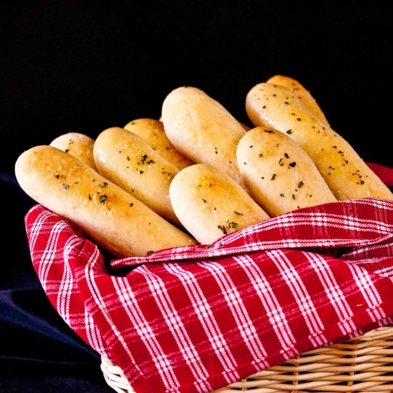 Homemade Olive Garden copycat breadsticks in a basket with a red striped towel.