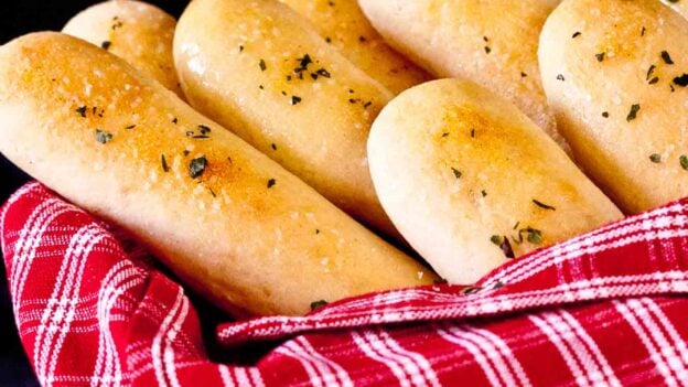 Homemade Olive Garden copycat breadsticks in a basket with a red striped towel.
