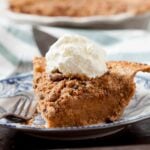 Closeup shot of sweet potato pecan pie slice on a blue pattern plate, with whipped cream on top.