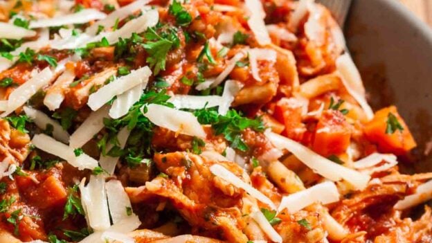Closeup shot of turkey bolognese topped with chopped parsley and shaved parmesan.