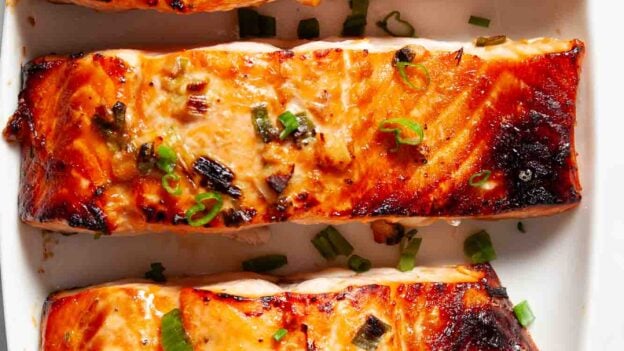 Overhead shot of Asian baked salmon fillets with chopped green onions on top.