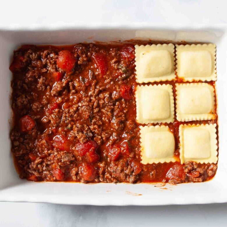 Ravioli casserole pasta and meat sauce being layered in pan.