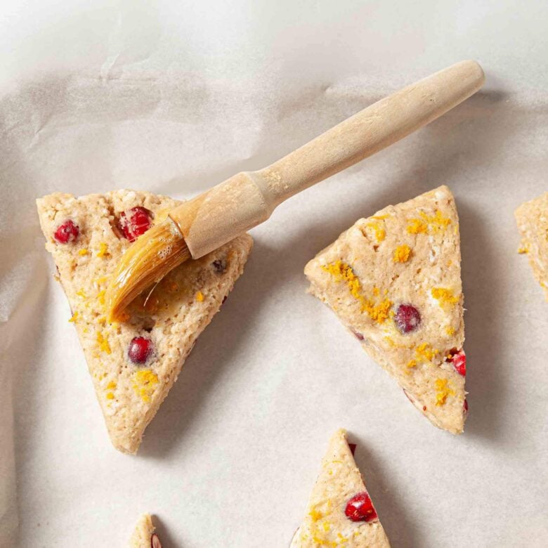 Cranberry orange scones being brushed with egg wash before baking.