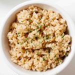 Overhead shot of a bowl of perfectly cooked instant pot brown rice, garnished with fresh herbs.