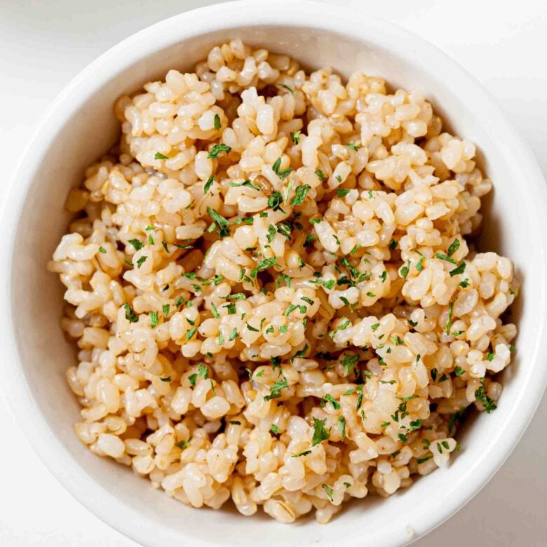 Overhead shot of a bowl of perfectly cooked instant pot brown rice, garnished with fresh herbs.