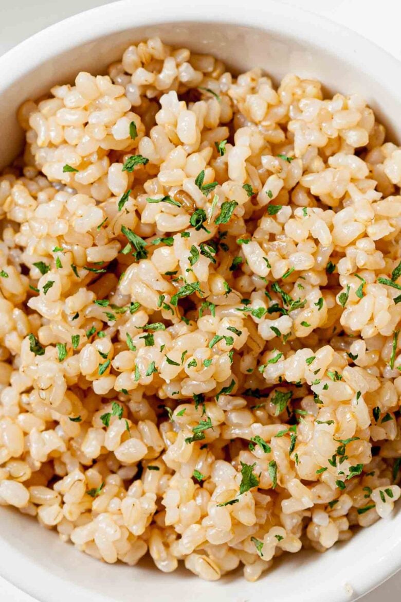 Overhead shot of a bowl of perfectly cooked instant pot brown rice, garnished with fresh herbs.
