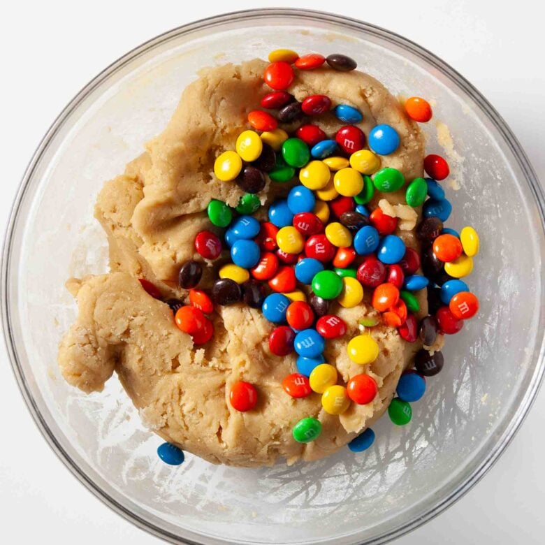 Colorful m&ms in cookie bar dough in a glass bowl.