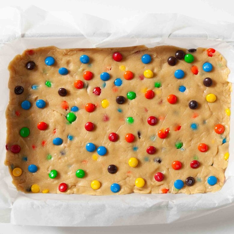 M&M cookie bar dough pressed into a lined baking tray, ready to be baked.