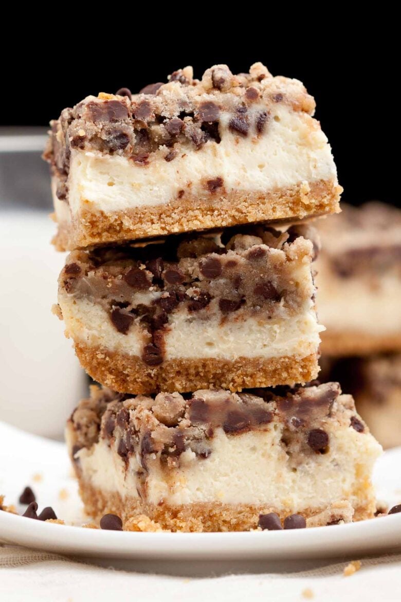 Three stacked Chocolate Chip Cheesecake Bars with a graham crust, creamy filling, and cookie topping are photographed close-up.