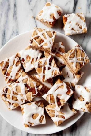 A plate of chewy Snickerdoodle Bars topped with white icing drizzle rests on a marble surface.