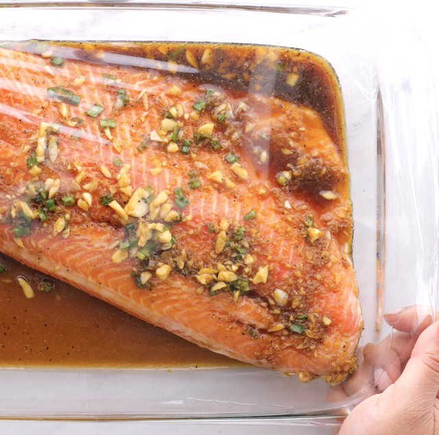 Salmon with marinade being covered with plastic wrap.