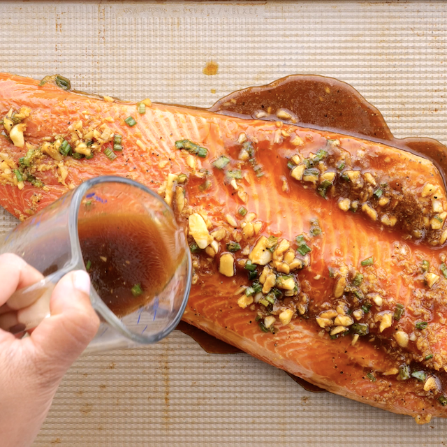 Leftover marinade being poured over salmon on a baking sheet.