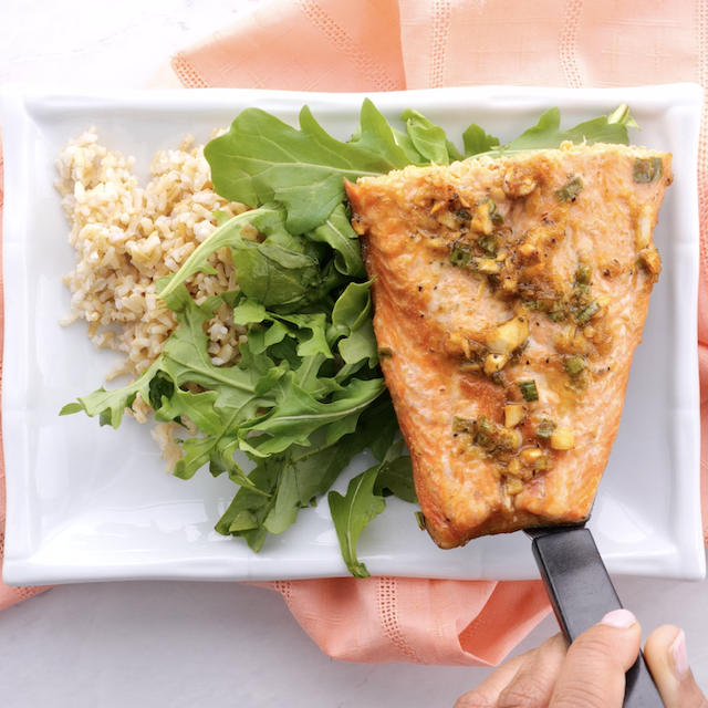 Freshly baked Asian baked salmon being served over rice and greens.