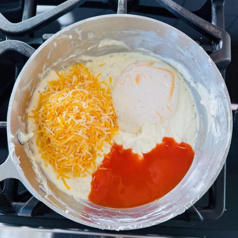 Ranch, hot sauce, and cheddar in a pot with melted cream cheese.