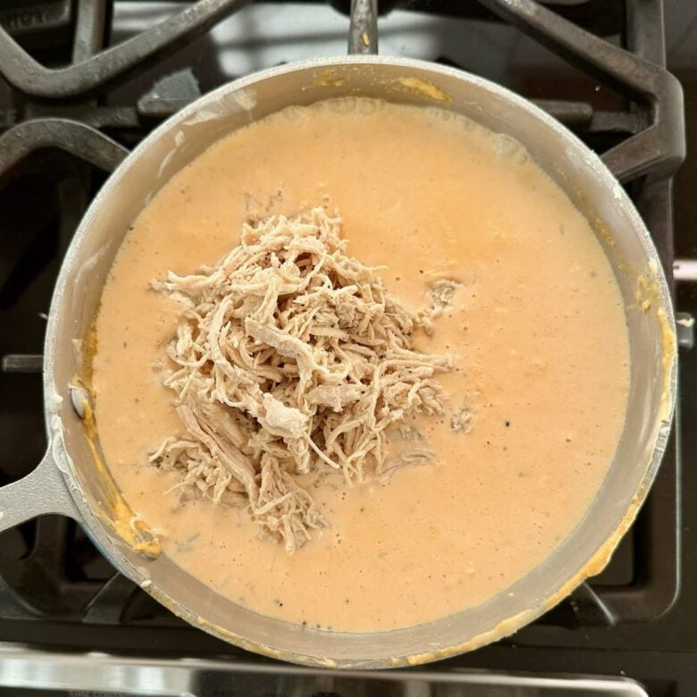 Shredded chicken added to buffalo chicken pasta sauce in a pot,